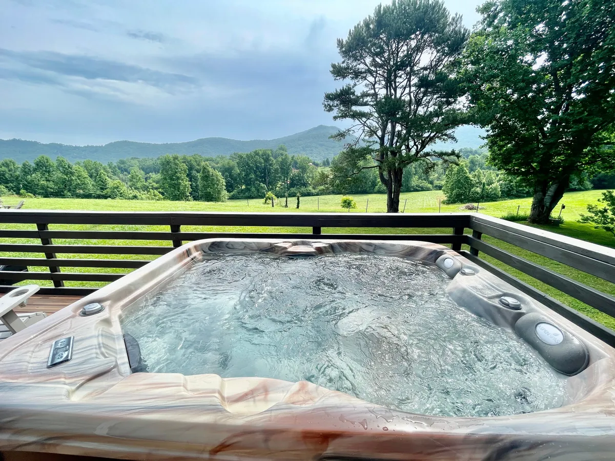 This image showcases a steaming hot tub set on a deck, overlooking a breathtaking panoramic mountain landscape. Lush greenery fills the foreground and distant mountain ridges stretch across the horizon, evoking tranquility and immersion in nature.