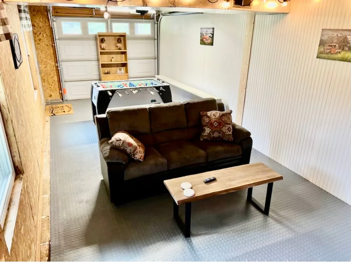 This image presents a game room setup with a comfy sofa, coffee table, prominent foosball table, and playful wall decor. The environment feels casual and social, ideal for group fun or watching TV together.