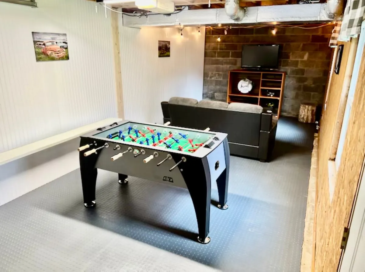 This image showcases a vibrant game room featuring a foosball table as the centerpiece, a comfortable sofa, TV, and wall art. The room's layout and decor highlight a fun, relaxed atmosphere perfect for game nights and casual gatherings.