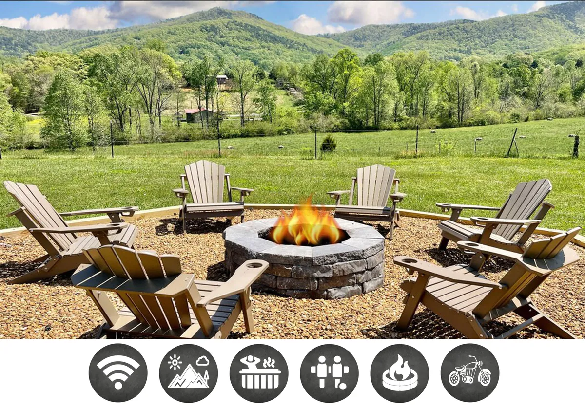 The image features the exterior of a cozy single-story cabin set against the lush green landscape of Wears Valley, Tennessee. Adirondack chairs circle a glowing fire pit, inviting guests to gather and relax. The scene is framed by sweeping mountain views under an open sky, capturing the perfect blend of comfort and wilderness.