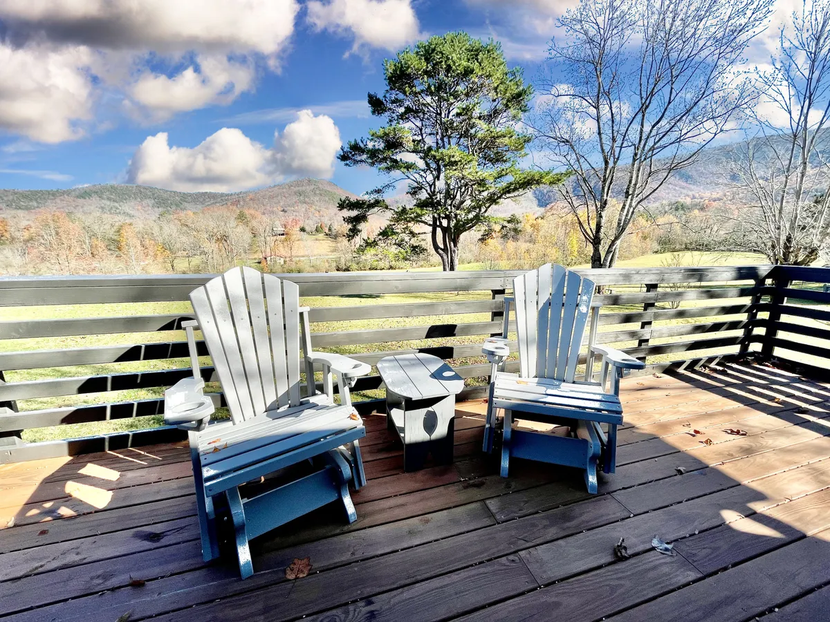 Two Adirondack chairs and a small table sit on a deck facing distant mountains, offering a peaceful spot for sunrise coffee, reading, or stargazing. The scene is serene, inviting you to soak in the untouched beauty of the Smokies.