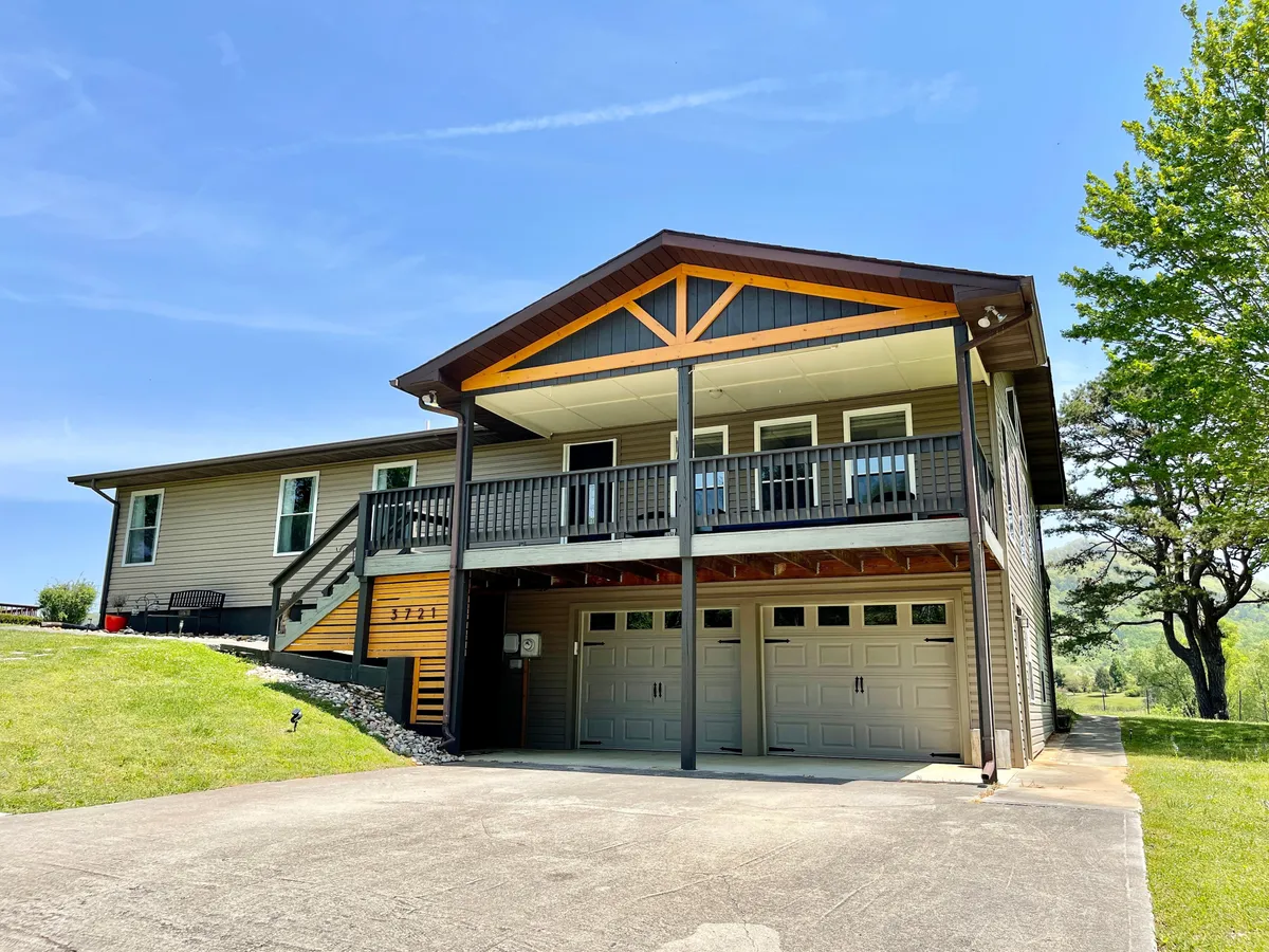 A large front porch with a peaked roofline overlooks a lush green lawn, creating a welcoming and spacious atmosphere. The inviting porch and balcony hint at communal family activities and relaxation outdoors, while the lawn provides space for children to play and families to gather.