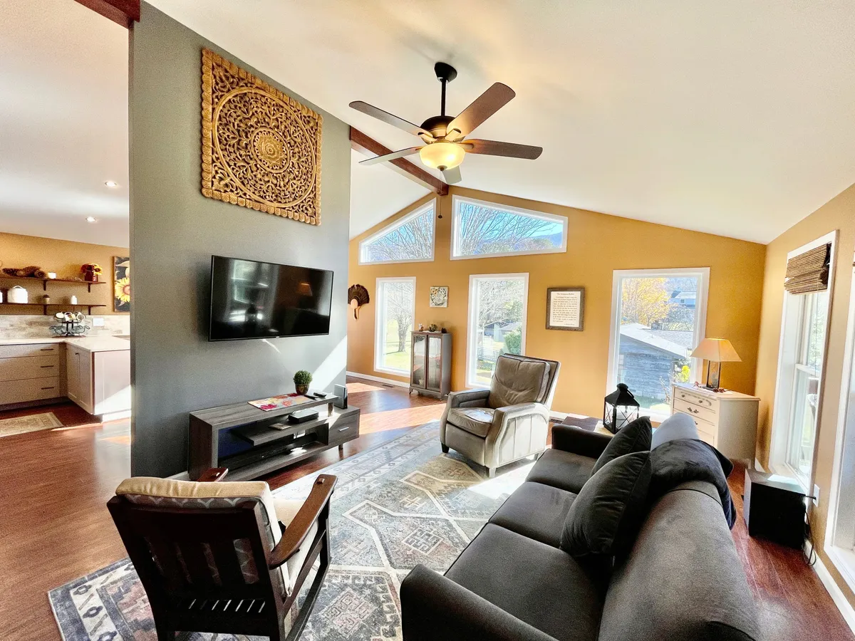 A cozy, inviting living space with a plush sofa facing a large TV. Decorative wall art, a wooden chair, and expansive windows frame the area, bringing in abundant natural light. The arrangement is perfect for movie nights, socializing, or quiet relaxation. The layout hints at a flexible space ideal for gatherings and family moments.