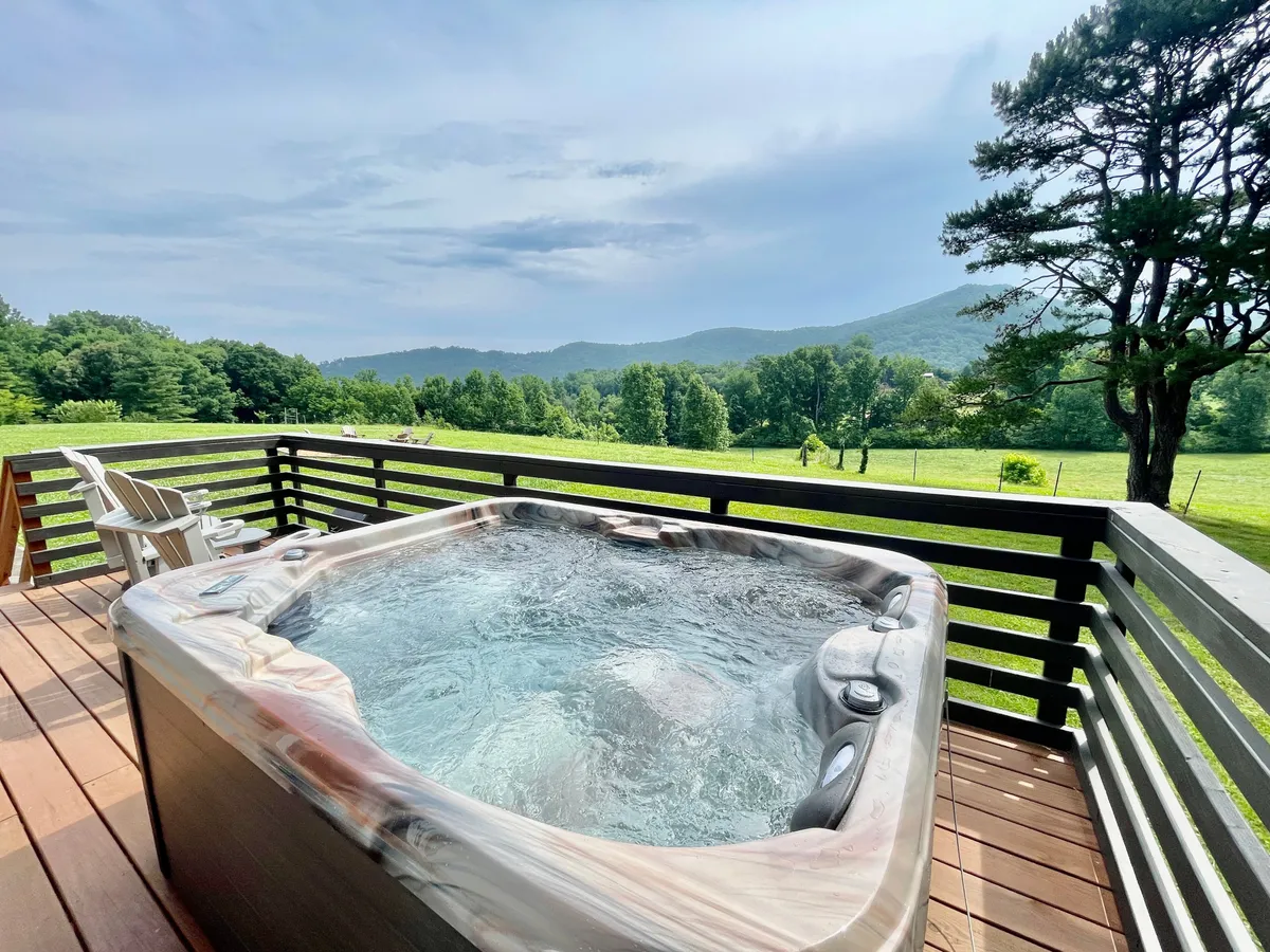 An inviting outdoor deck featuring a bubbling hot tub with panoramic mountain views and lush greenery all around. The scene suggests a perfect spot for relaxing after a day of activities, with space for multiple people to unwind together under the open sky.