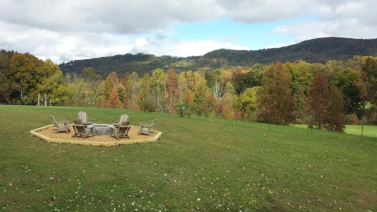 The image showcases a fire pit set among Adirondack chairs, surrounded by trees and boasting an expansive mountain view. The setting is designed for relaxing evenings, stargazing, and soaking up the stunning Smoky Mountain backdrop.