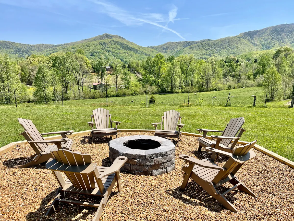A cozy exterior fire pit area framed by Adirondack chairs and expansive mountain views, set on green grass. The setup is inviting for gatherings, storytelling, stargazing, and enjoying tranquil outdoor evenings.