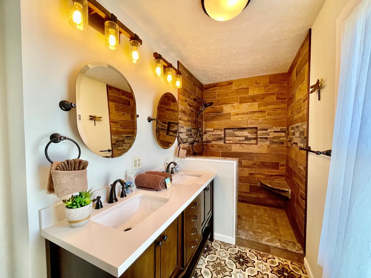 A modern and refreshing bathroom with a double sink vanity, bright mirrors, a walk-in shower, decorative tile flooring, and contemporary lighting fixtures. The space feels clean and well-appointed, perfect for both morning and evening routines.